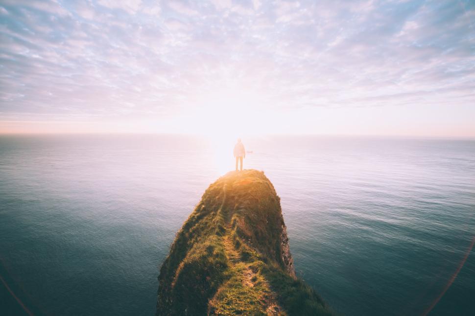 Free Image of Man standing on cliff edge looking at serene ocean sunset. 