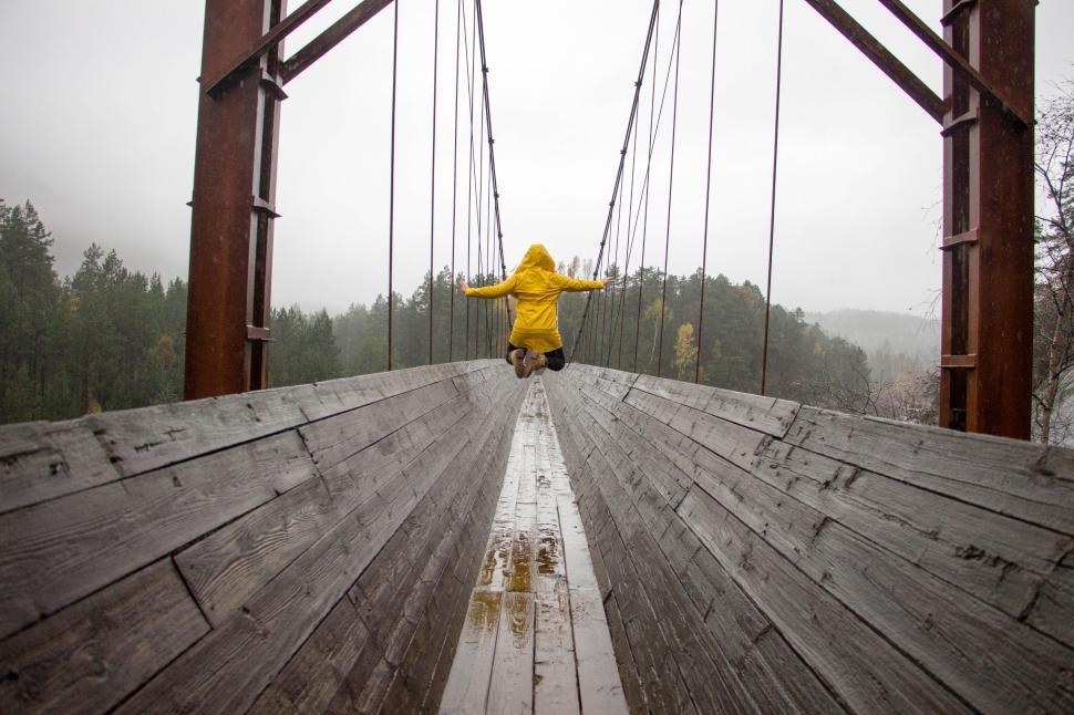 Free Image of Person jumping on a suspended bridge in yellow raincoat 
