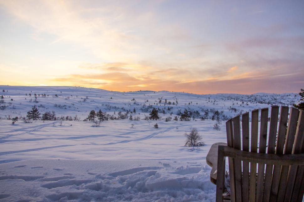 Free Image of Serene snowy landscape with sunset and wooden chair 