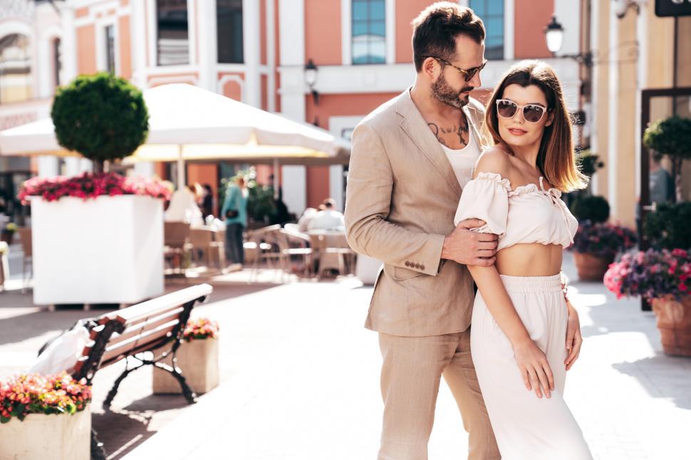 Free Image of Couple enjoying a stylish afternoon in a vibrant plaza adorned with flowers and bustling cafes 