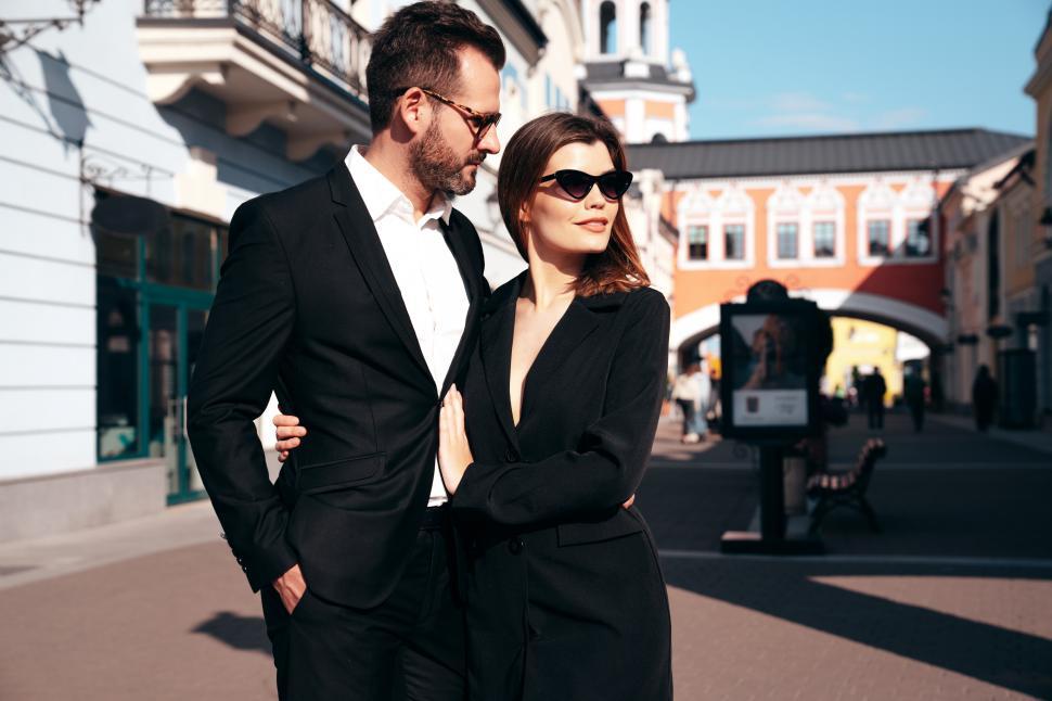 Free Image of Stylish couple enjoys a sunny day in a charming urban setting while dressed in elegant formal attire 