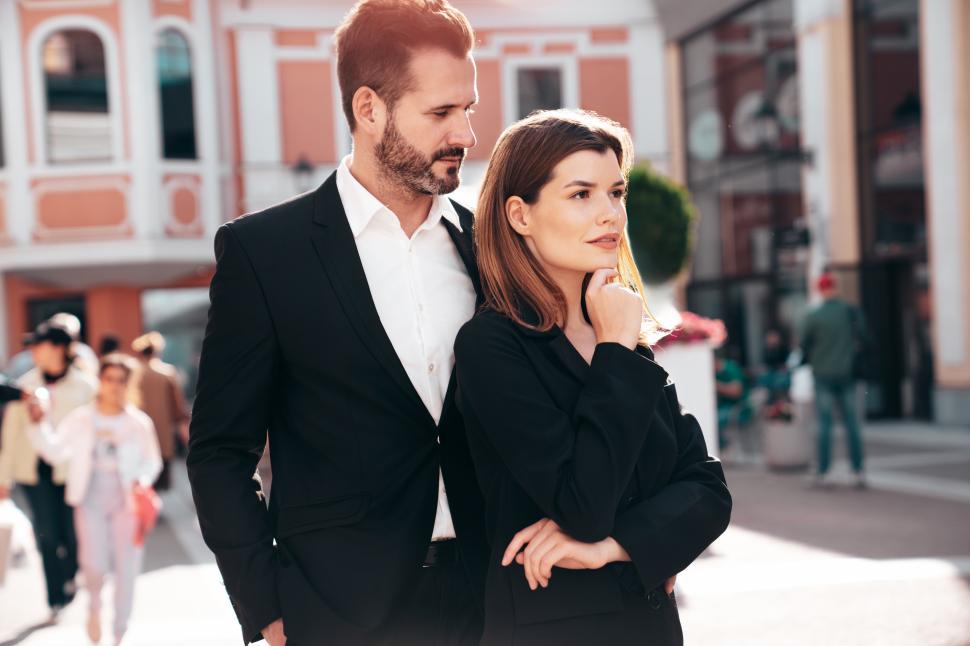 Free Image of Couple dressed in formal attire standing confidently in a busy urban area during daylight hours 