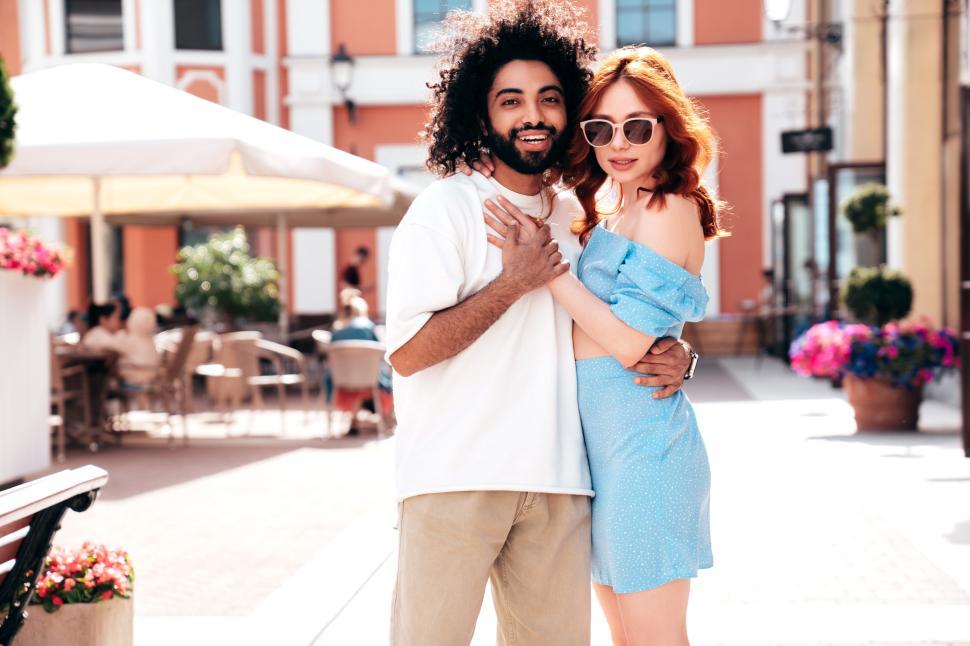 Free Image of Couple enjoying a sunny day together in a vibrant outdoor plaza with colorful buildings and flowers 