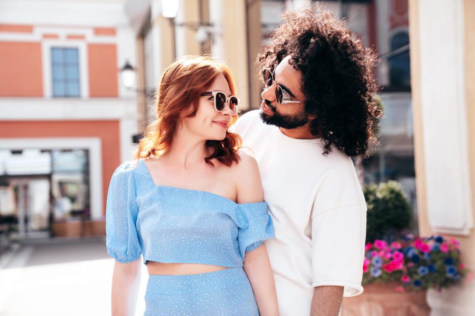 Free Image of Couple enjoying a sunny day while walking together in a charming street with colorful buildings and flowers around 