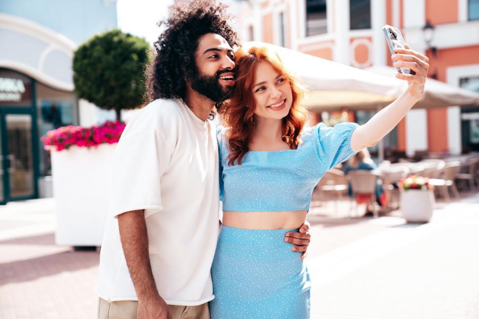 Free Image of Friends enjoy a sunny day while taking selfies in a vibrant outdoor plaza filled with colorful cafes and shops 