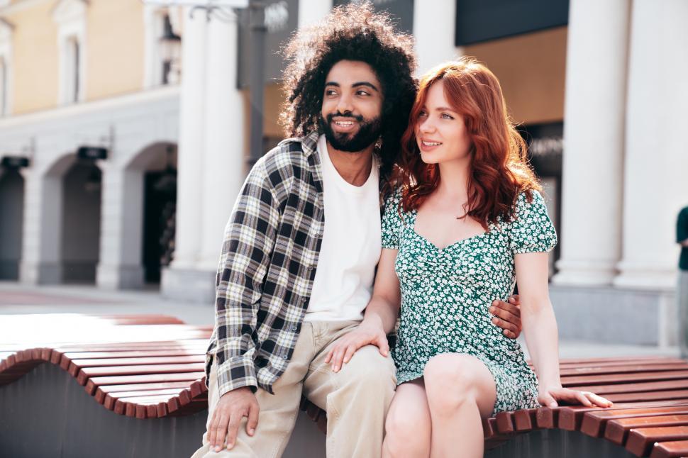 Free Image of Smiling couple enjoying a sunny day in a vibrant urban park while sitting on a wooden bench 