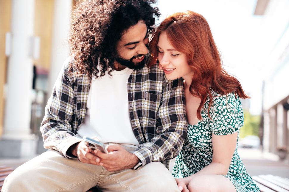 Free Image of Couple enjoys a sunny day outdoors while sharing a moment on a bench in a vibrant city 