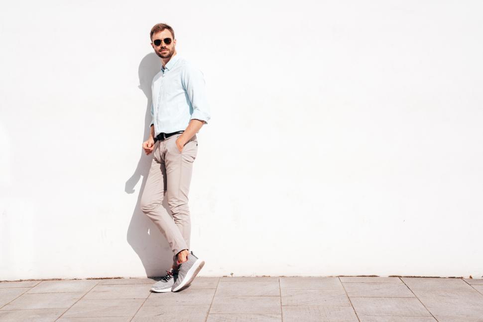 Free Image of Stylish man leans against a minimalistic white wall during daylight in an urban setting 