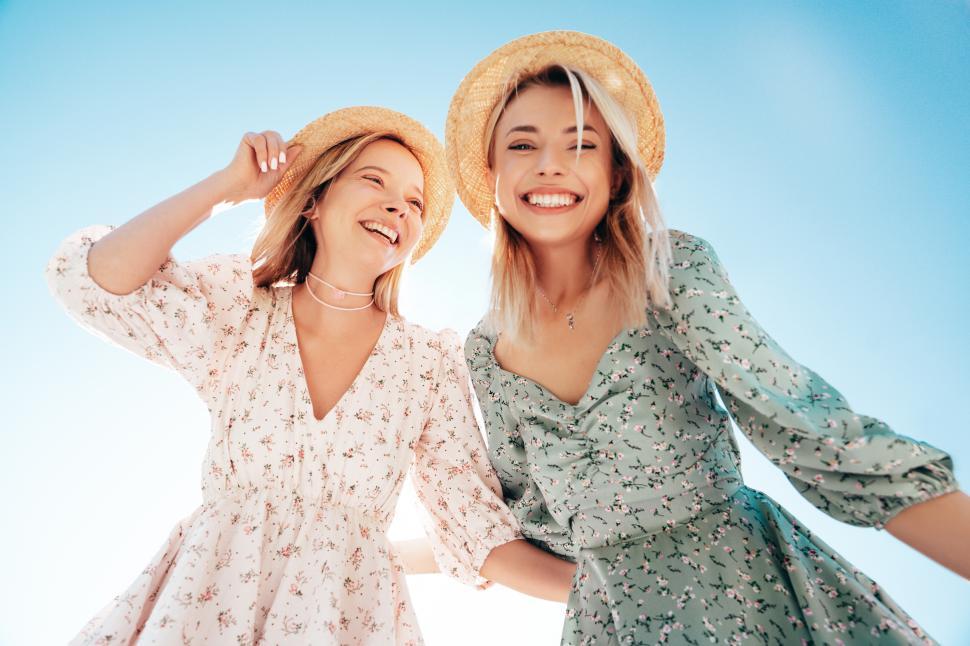 Free Image of Friends enjoy a sunny day outdoors wearing summer dresses and straw hats while smiling and posing for a fun moment together 