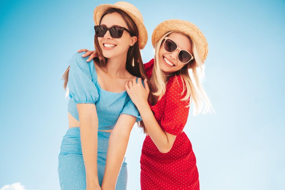 Free Image of Friends enjoy a sunny day outdoors while wearing bright outfits and sunglasses in a tropical setting 