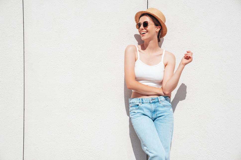 Free Image of Young woman enjoying a sunny day while leaning against a white wall in casual summer clothing 