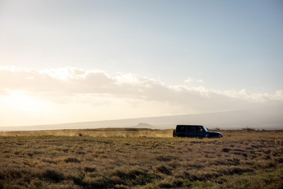 Free Image of SUV driving through vast open landscape at sunset time 