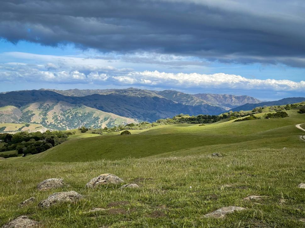 Free Image of Wide view of rolling green hills under a cloudy sky. 
