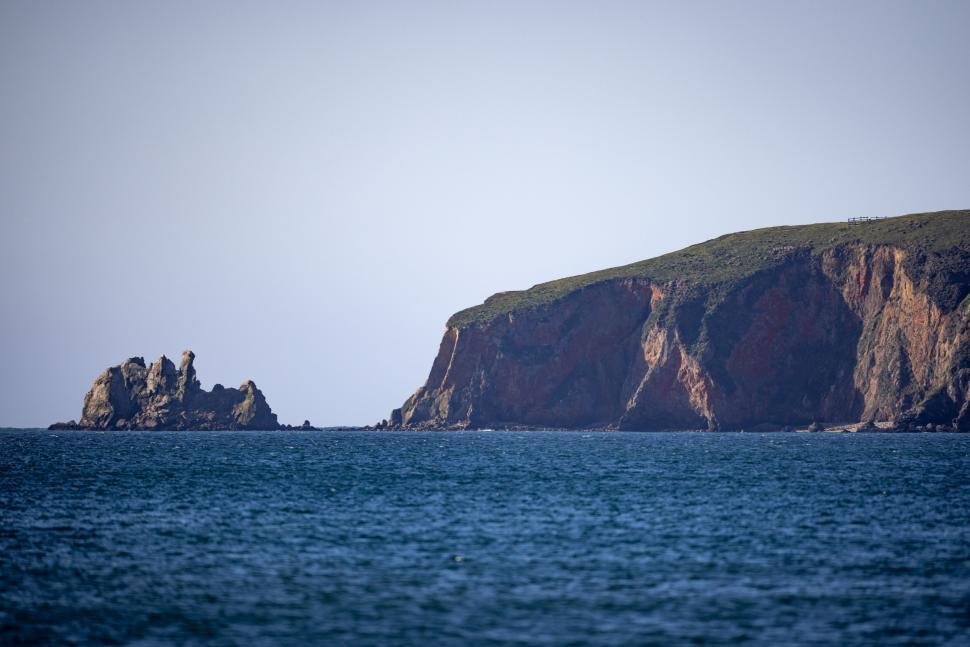 Free Image of Rocky coastal cliff with blue sea and sky background 