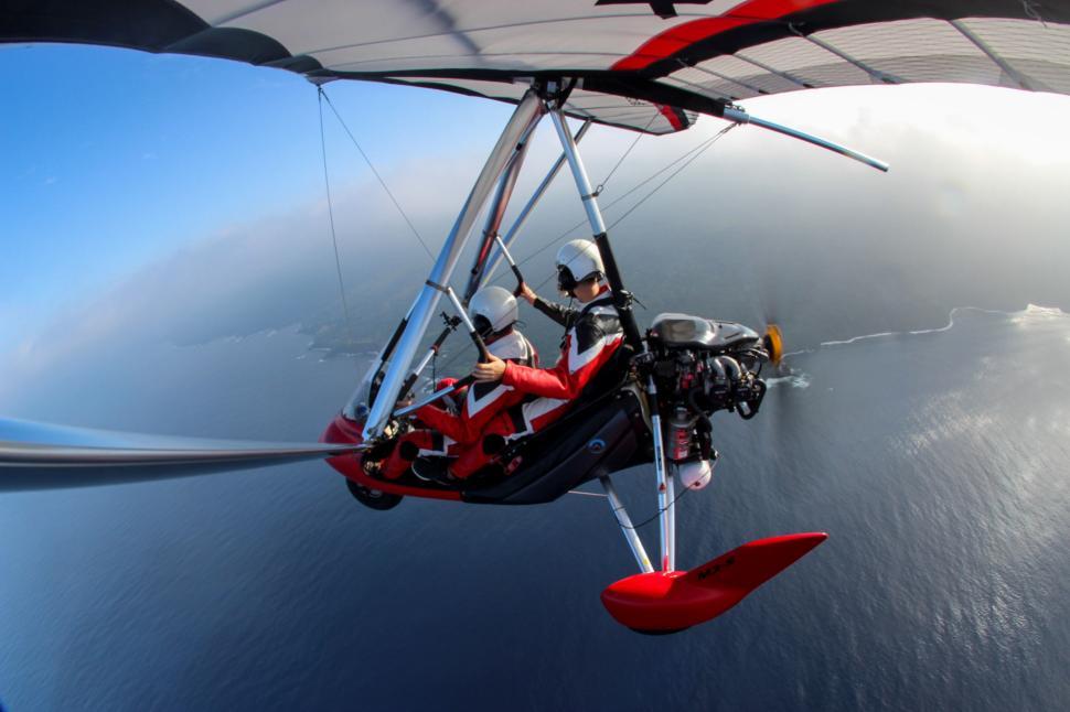 Free Image of Adventurers in a motorized hang glider soaring over ocean. 