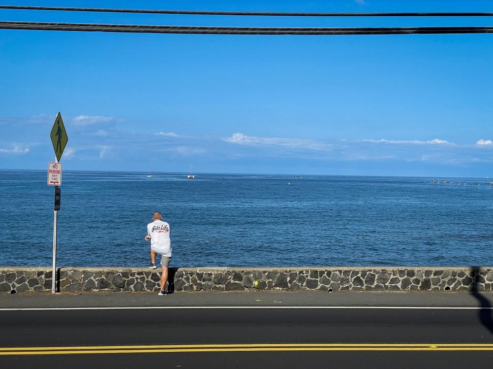 Free Image of A person leaning on a stone wall overlooking big ocean 