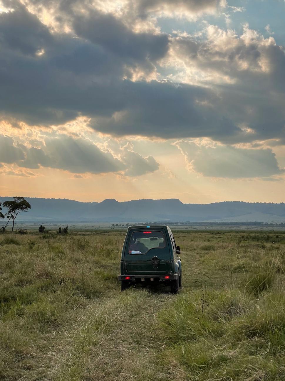 Free Image of A small vehicle driving through grassy field at sunset 