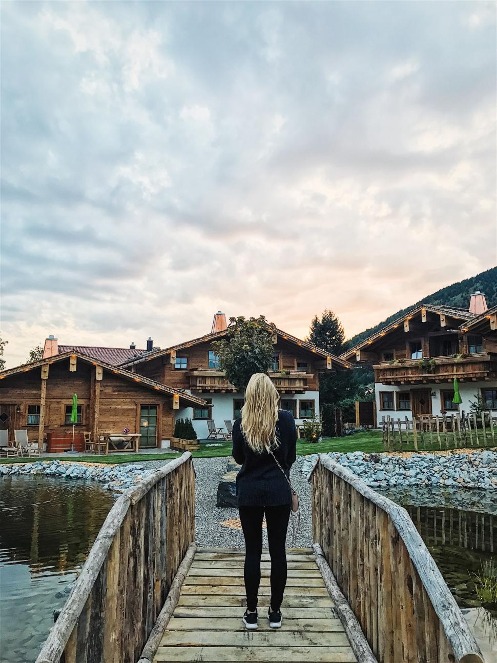 Free Image of Woman on wooden bridge overlooking charming wooden cabins. 