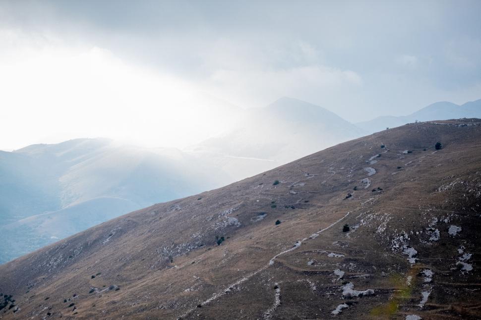 Free Image of Sunlight piercing through clouds over rolling hills 