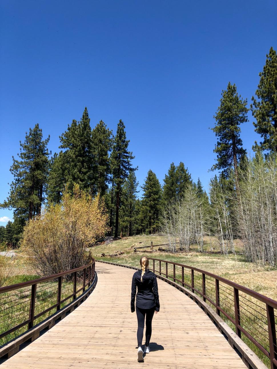 Free Image of Person walking on wooden boardwalk under a clear sky. 
