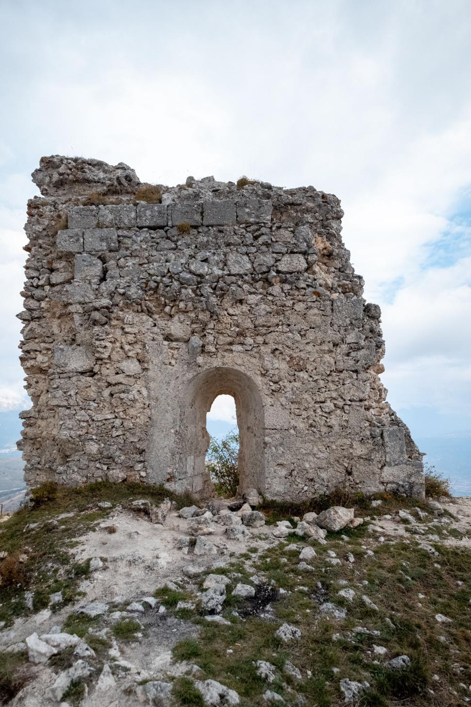 Free Image of Ancient stone ruin with archway on grassy hilltop 