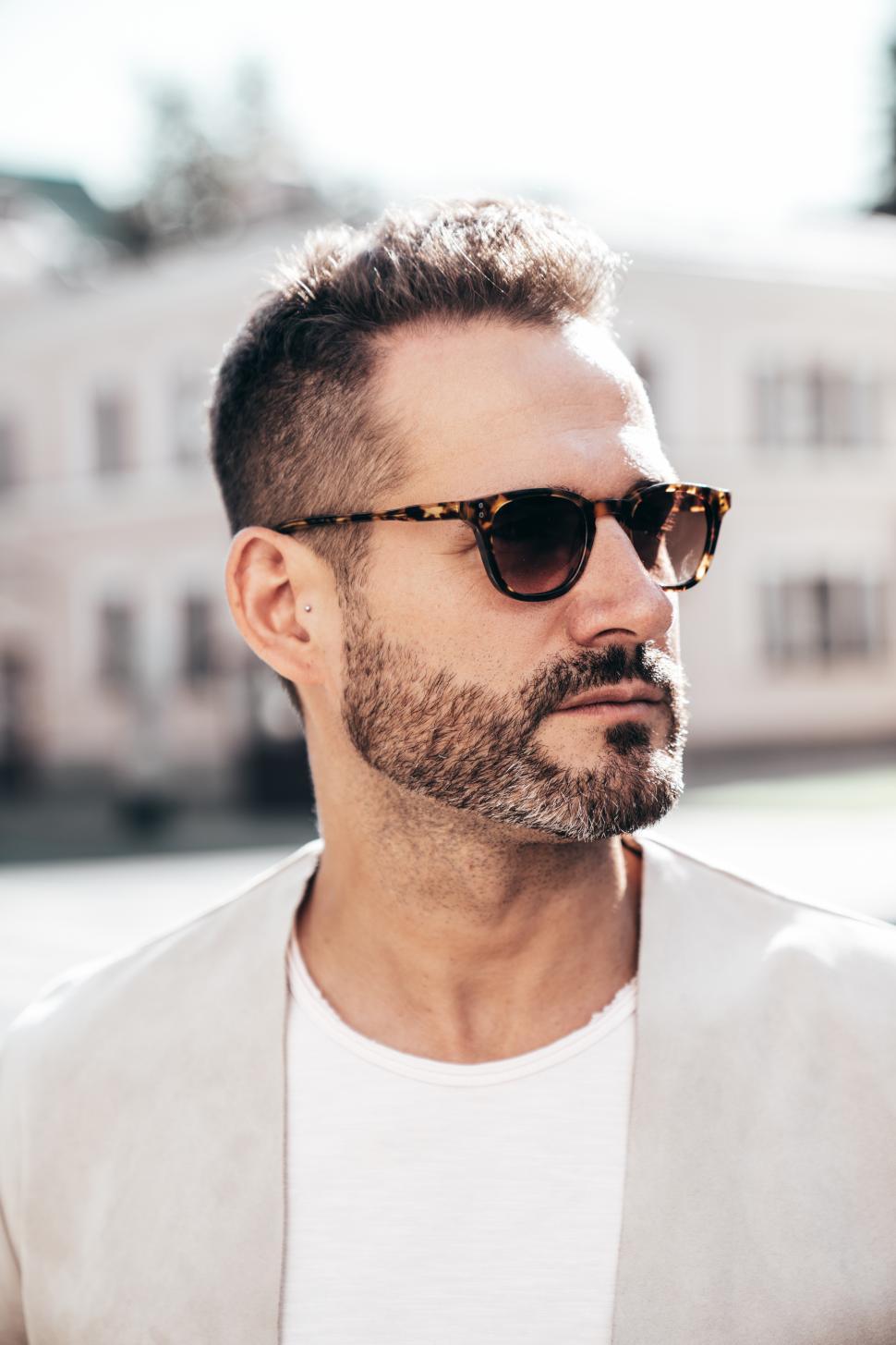 Free Image of Stylish man wearing sunglasses outdoors in bright sunlight on a warm day during a casual city stroll 