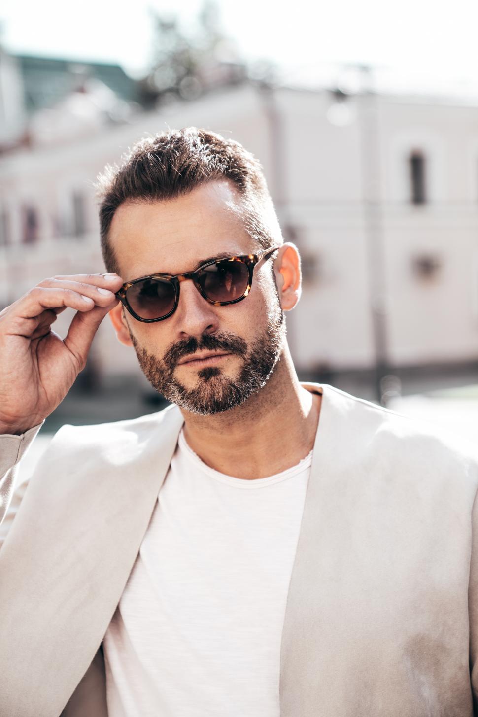 Free Image of Confident man adjusting sunglasses while standing outdoors in city during daylight 