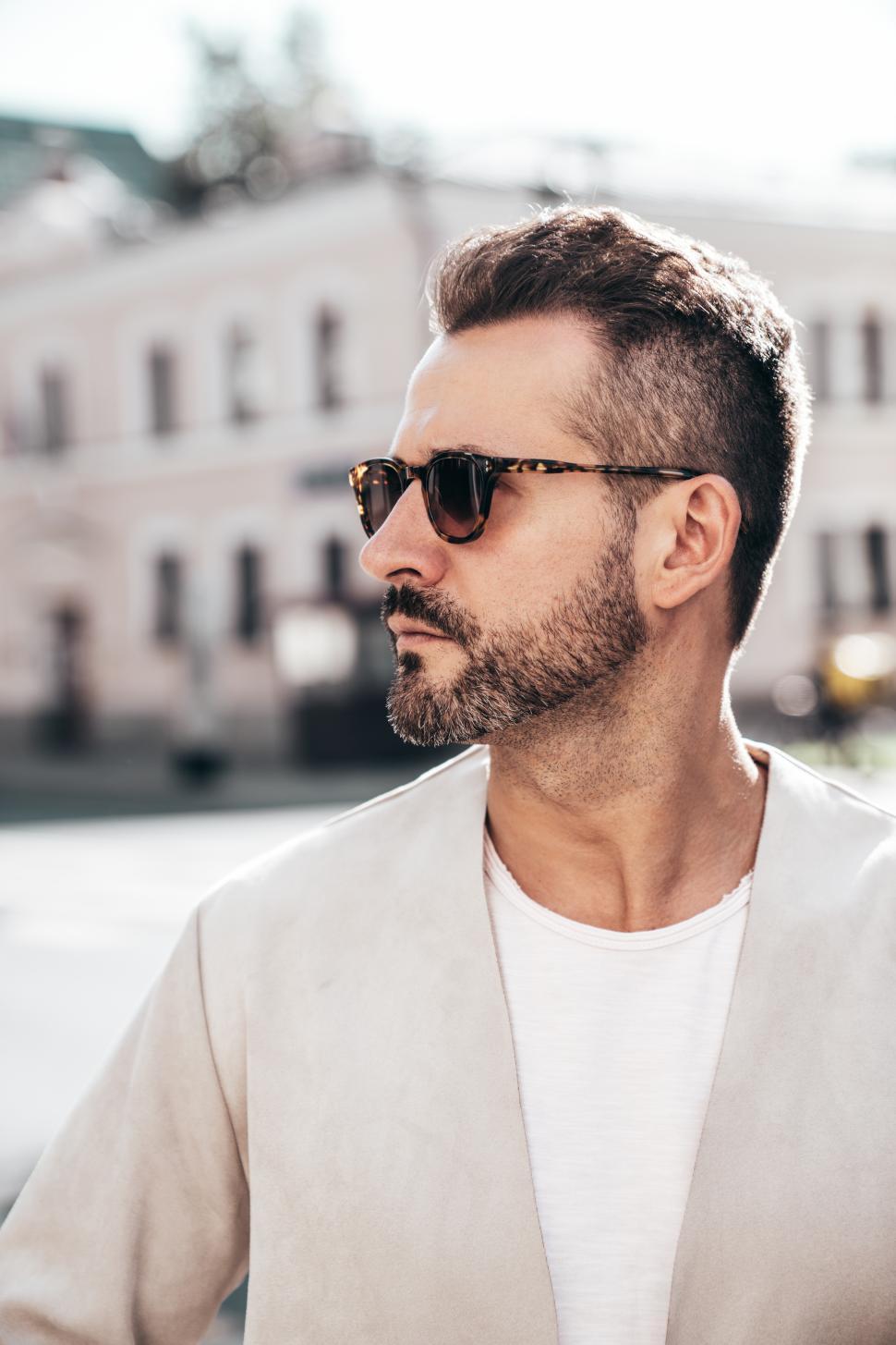 Free Image of Stylish man wearing sunglasses poses confidently in urban setting during sunny day 