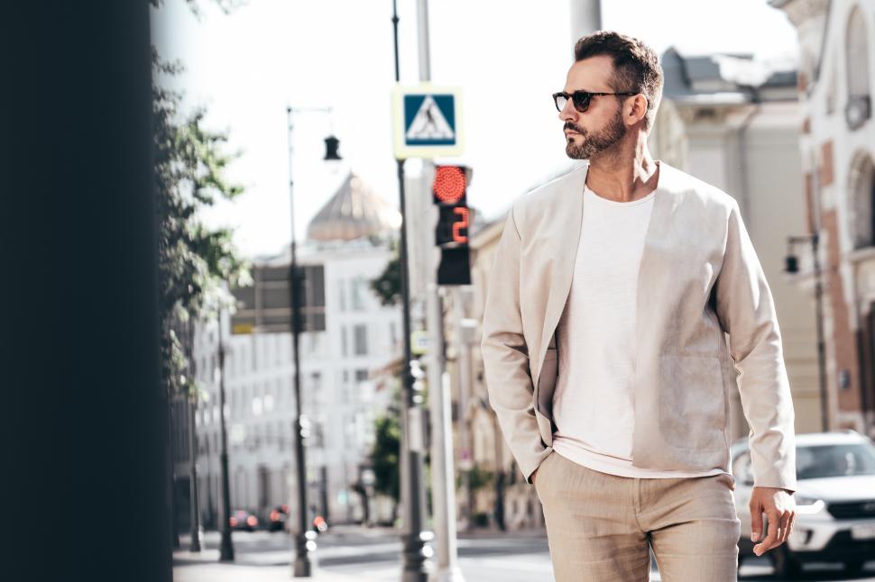 Free Image of Stylish man walking through a city street on a sunny day in a modern outfit with sunglasses and a confident demeanor 