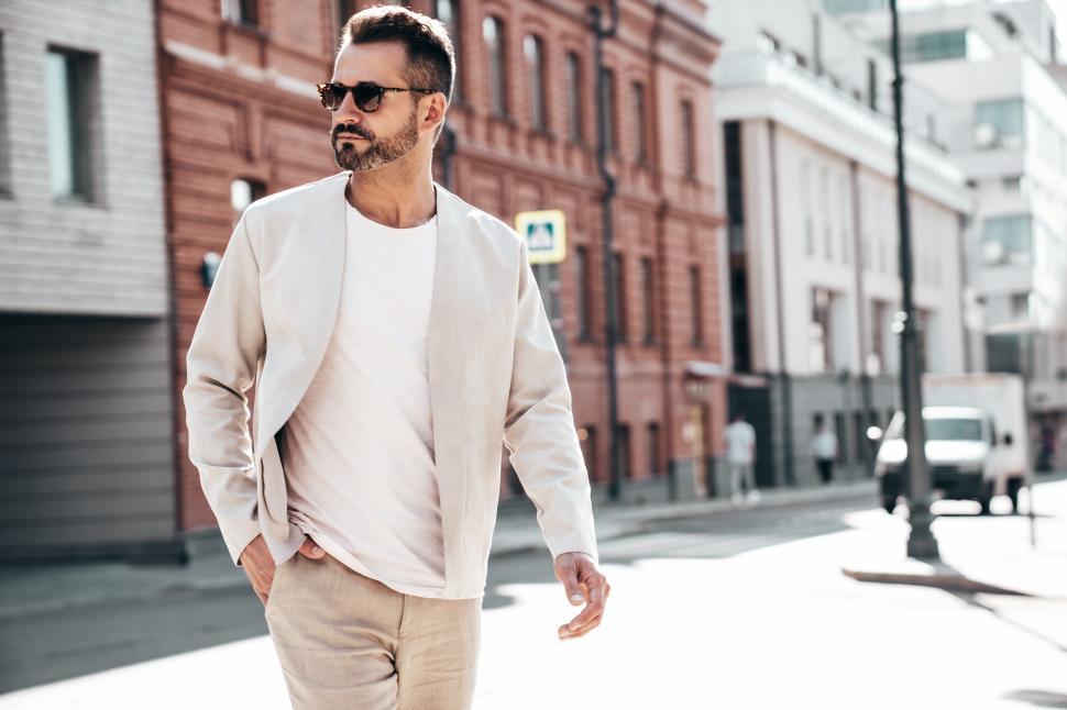 Free Image of Man in stylish outfit walks confidently along city street in daylight near modern buildings 