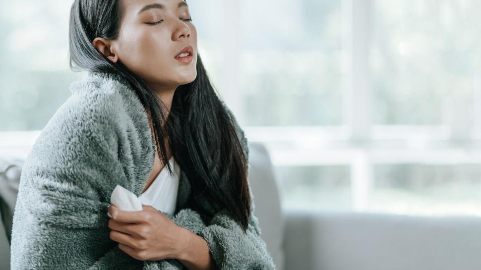 Free Image of Unhappy sad Asian woman in cloak suffering from fever and flu on sofa 