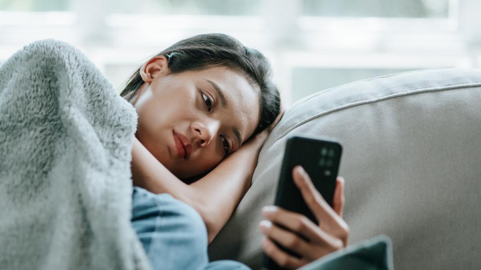Free Image of Asian woman in bed suffering from fever and flu on sofa while using mobile phone 