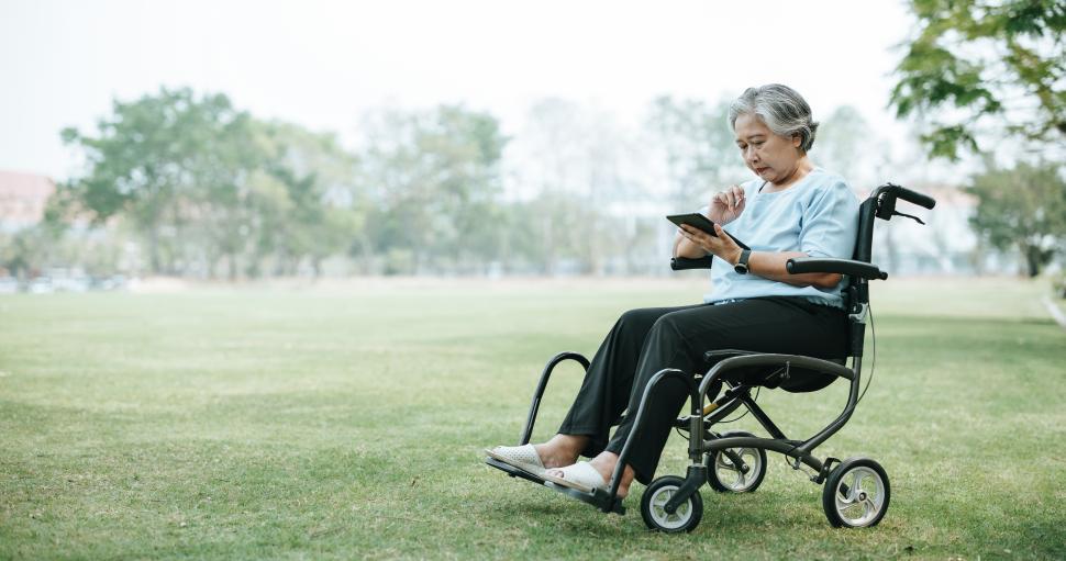 Free Image of Mature Asian woman on wheelchair use tablet at grass field 