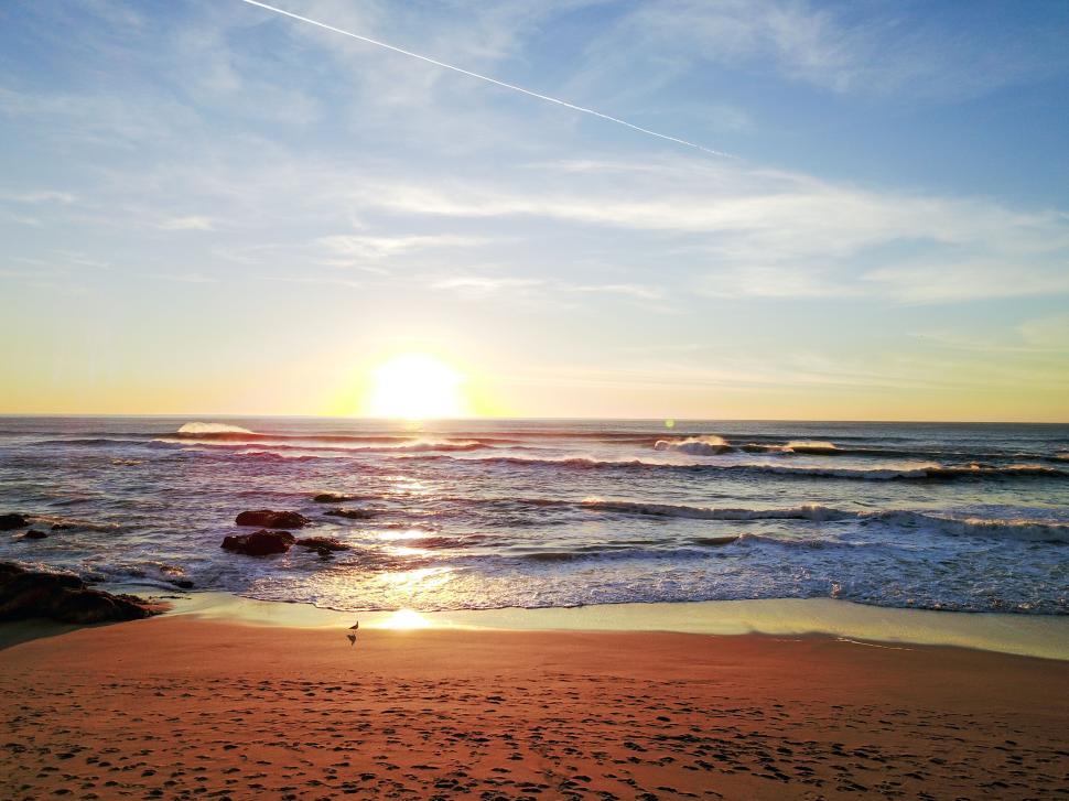 Free Image of Sunset over the ocean with waves and sandy beach. 
