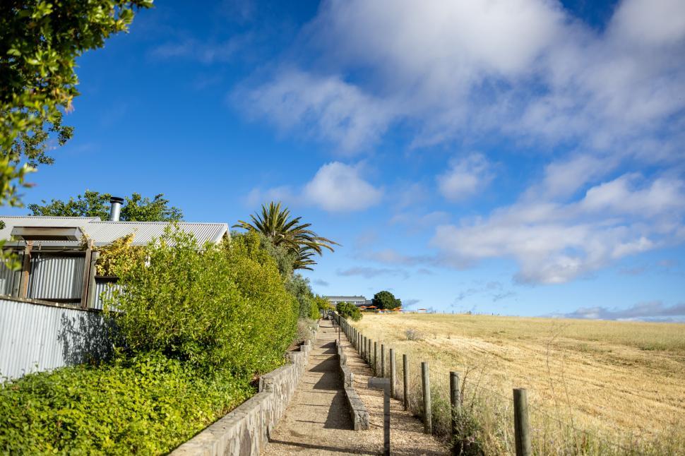 Free Image of Rural pathway beside a house with a blue cloudy sky 