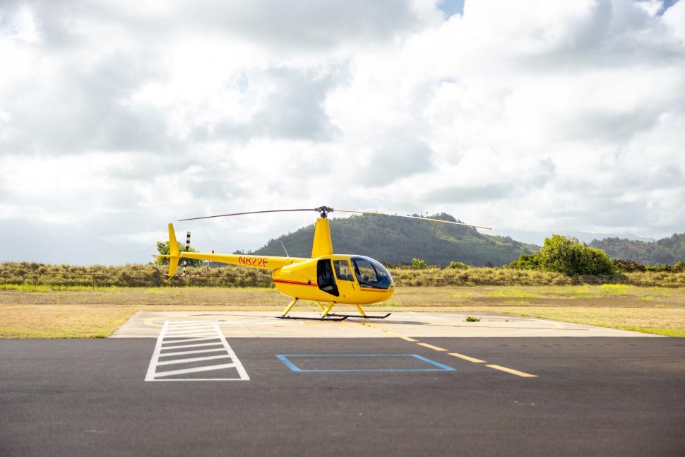 Free Image of Yellow helicopter parked on airstrip with mountains behind 