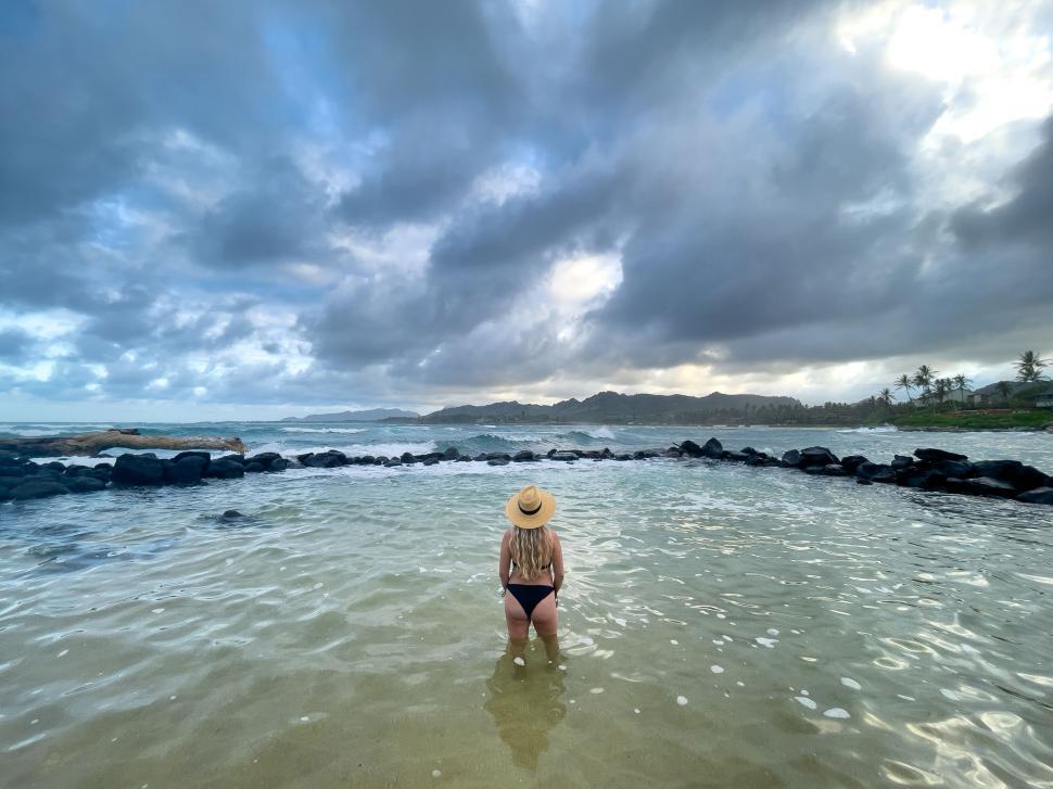 Free Image of Woman standing in shallow ocean water under cloudy sky 