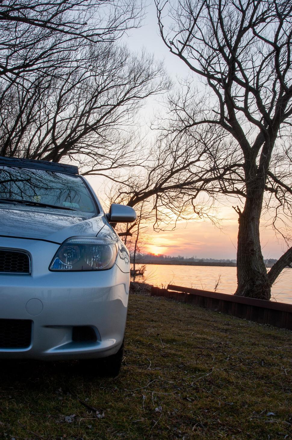 Free Image of Car parked under leafless trees near a river at sunset. 
