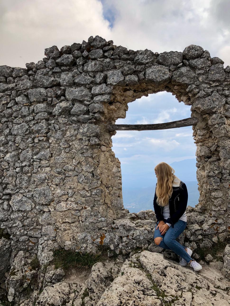 Free Image of Woman sitting by ancient stone ruin window with view 
