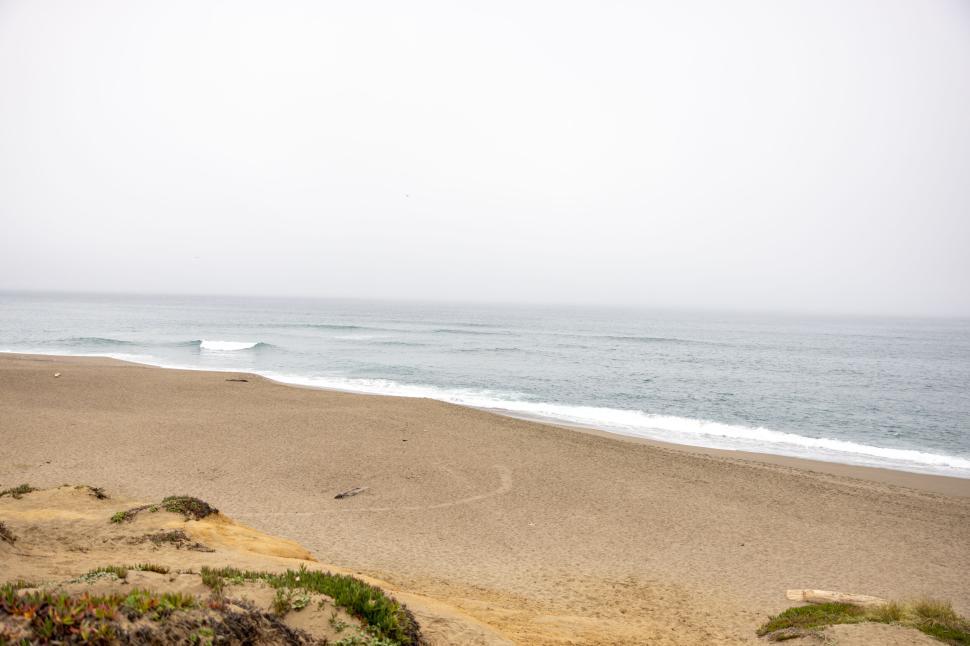Free Image of Empty beach with gentle waves under a overcast sky 