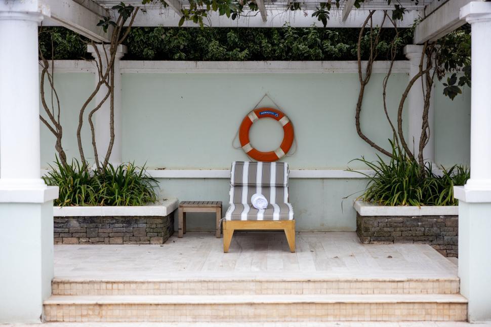 Free Image of Striped chaise lounge under pergola beside life preserver ring. 