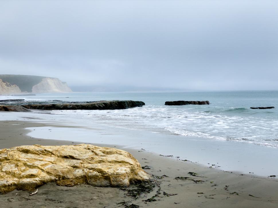 Free Image of Coastal scene with cliffs meeting the ocean under grey skies. 