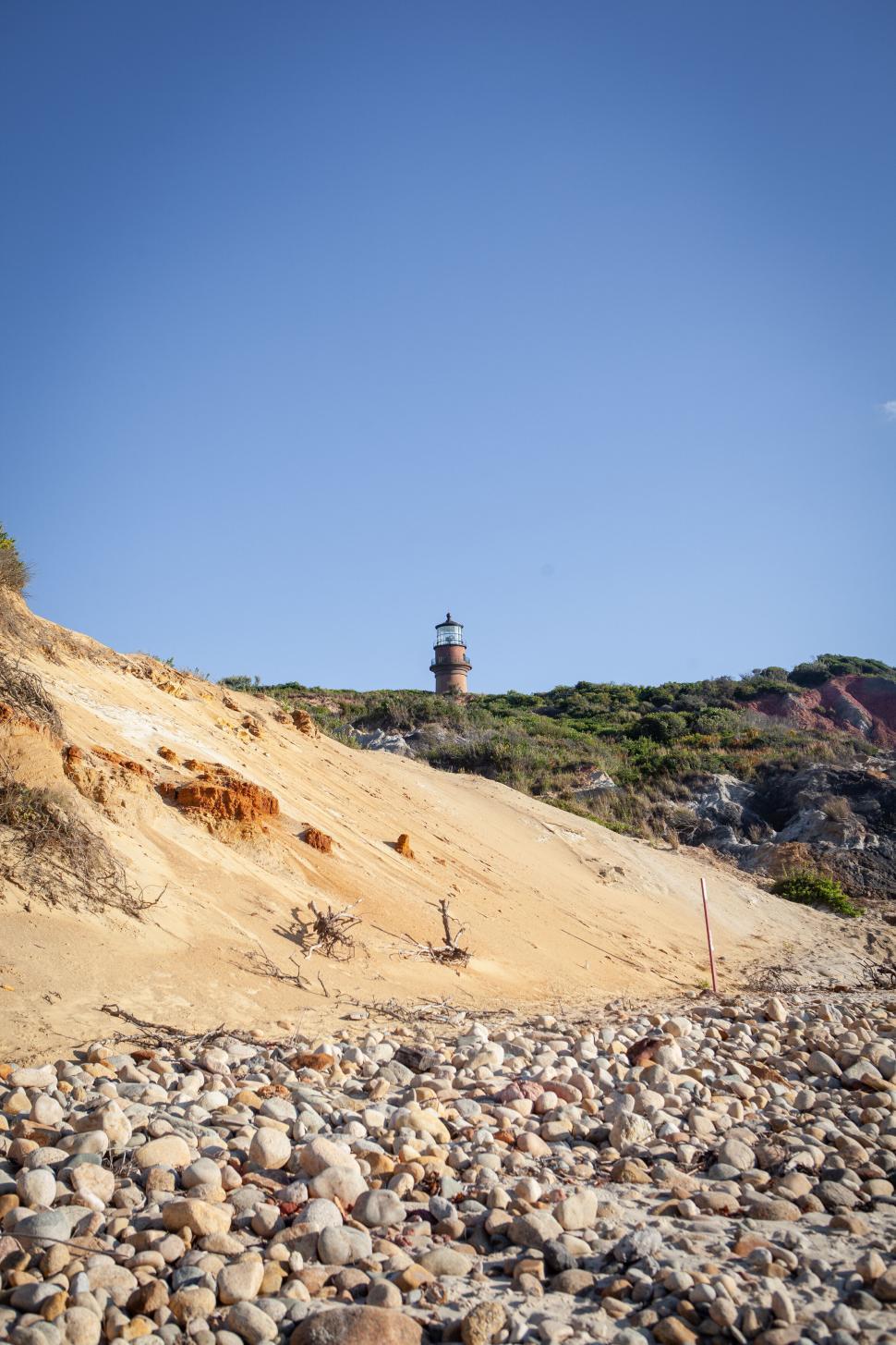 Free Image of Lighthouse atop rocky hillside under clear blue sky. 