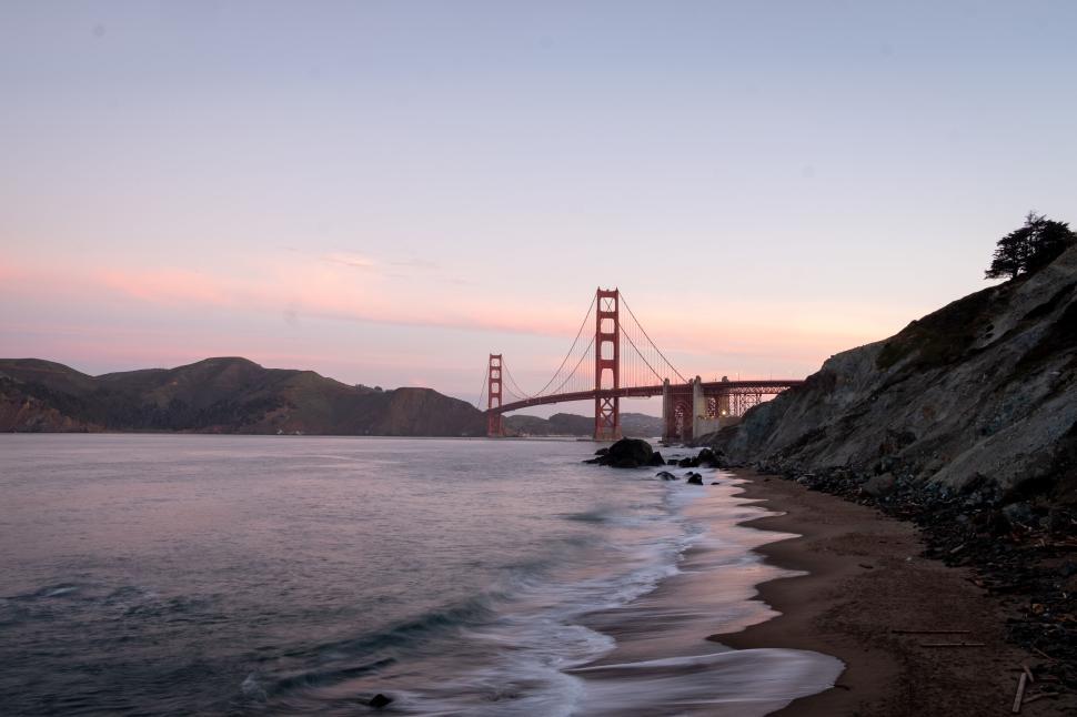 Free Image of Golden Gate Bridge at sunset with calm beach in sight. 