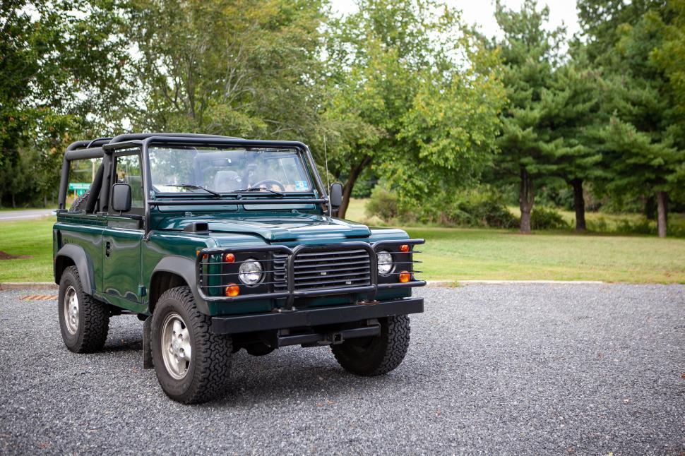 Free Image of Classic green 4x4 jeep in front of lush forest trees. 