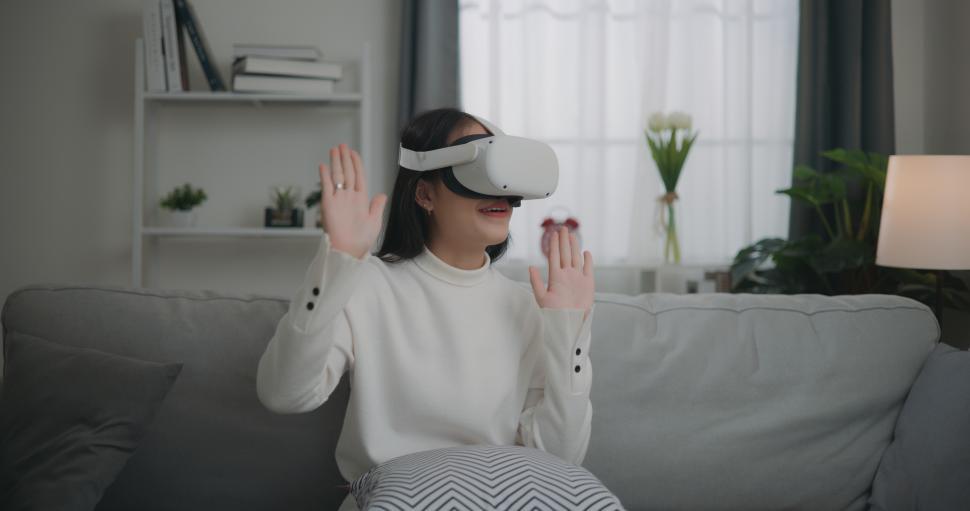 Free Image of Asian woman watching a concert via VR glasses and dancing while sitting on the sofa 
