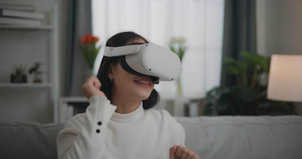 Free Image of Asian woman watching a concert via VR glasses and dancing while sitting on the sofa 
