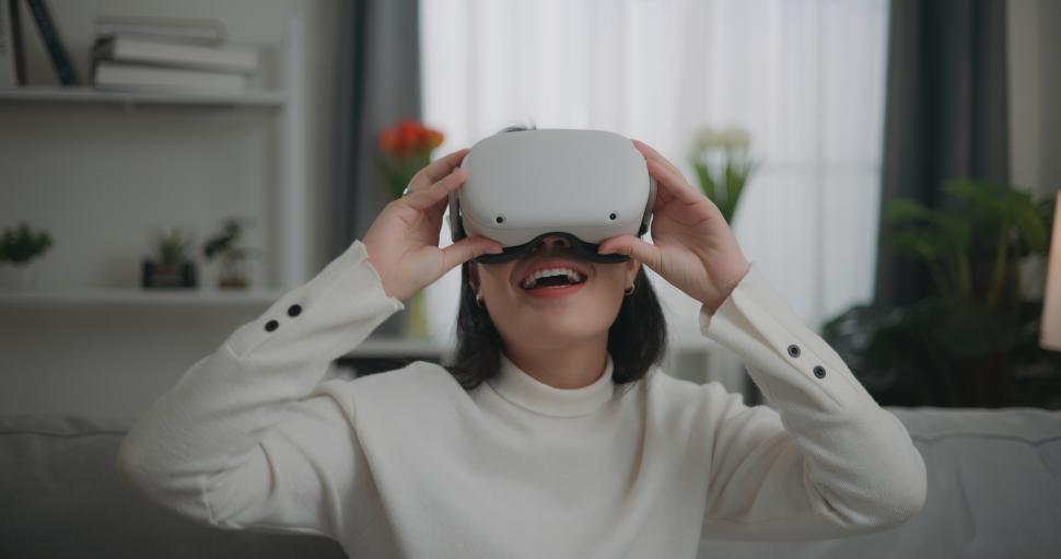 Free Image of Asian woman watching a concert via VR glasses and dancing while sitting on the sofa 