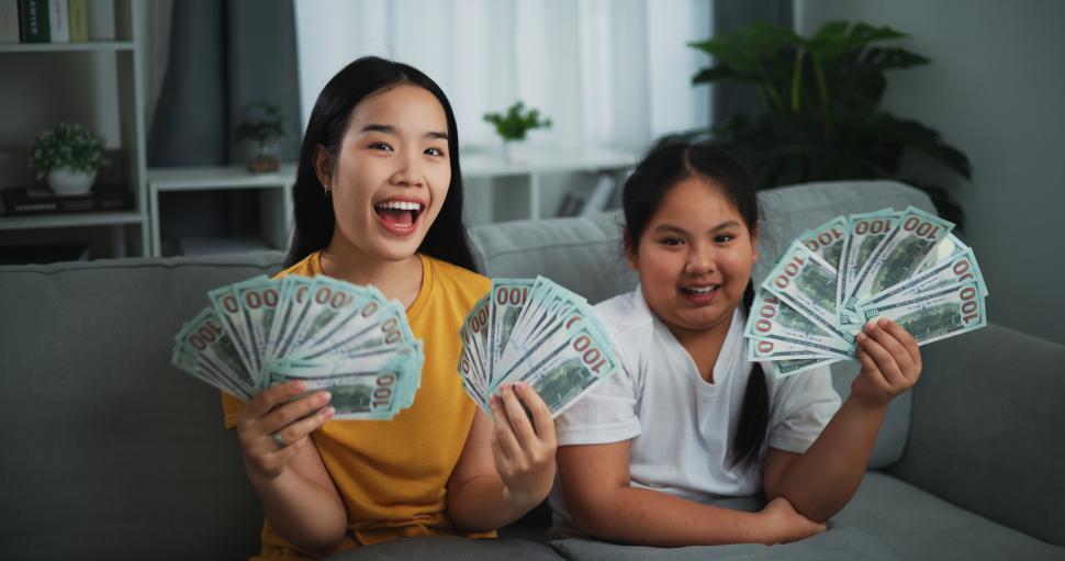 Free Image of Portrait of young Asian woman showing dollar at camera and smiling on sofa in the living room at home. 