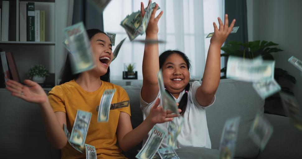 Free Image of Portrait of a young woman and teenage girl enjoying scattering cash bills on a sofa in the living room at home. 